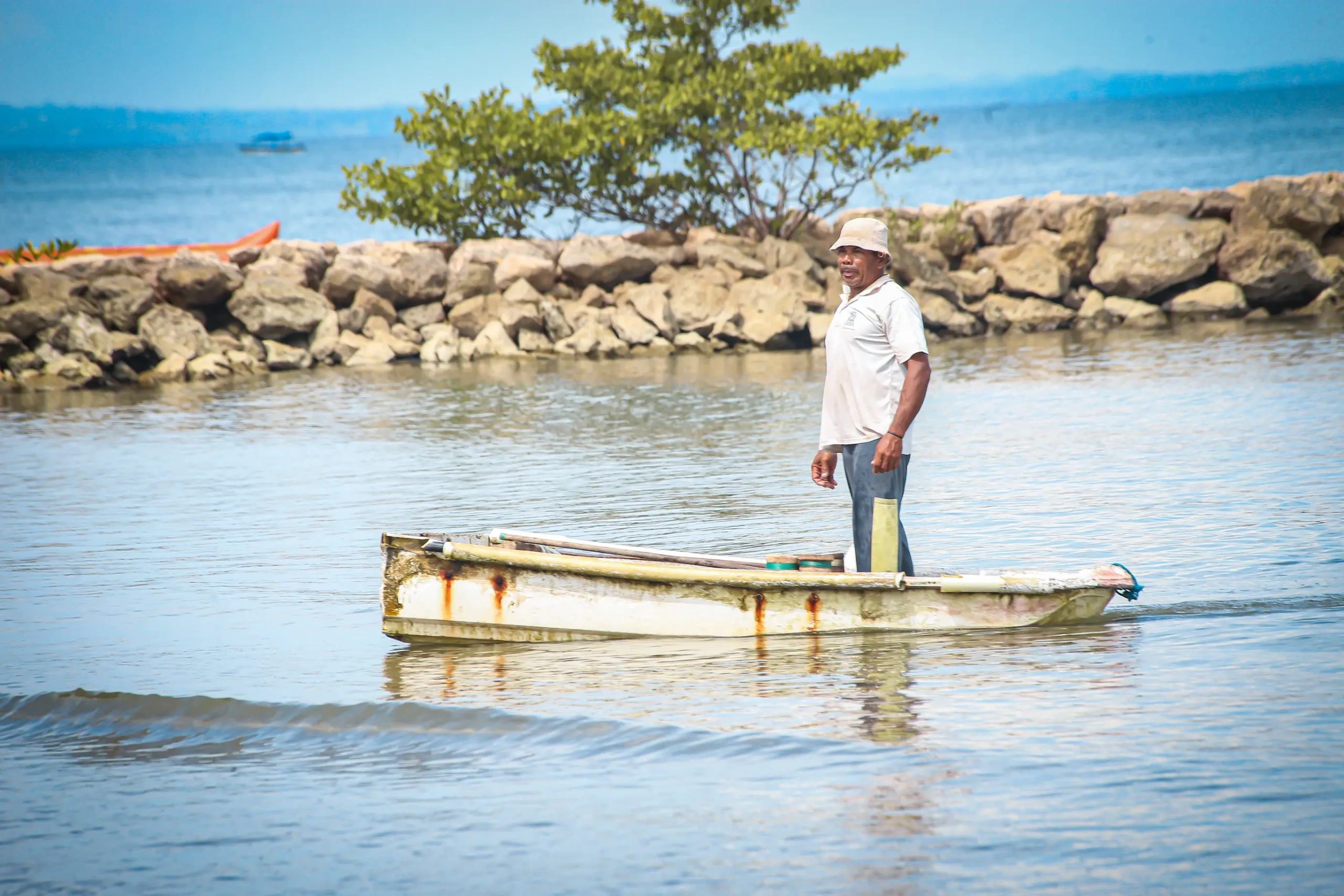 Tres pescadores artesanales en canoa lanzando redes en un río, con exuberante vegetación en las orillas, bajo un cielo claro en el departamento de Sucre, Colombia.